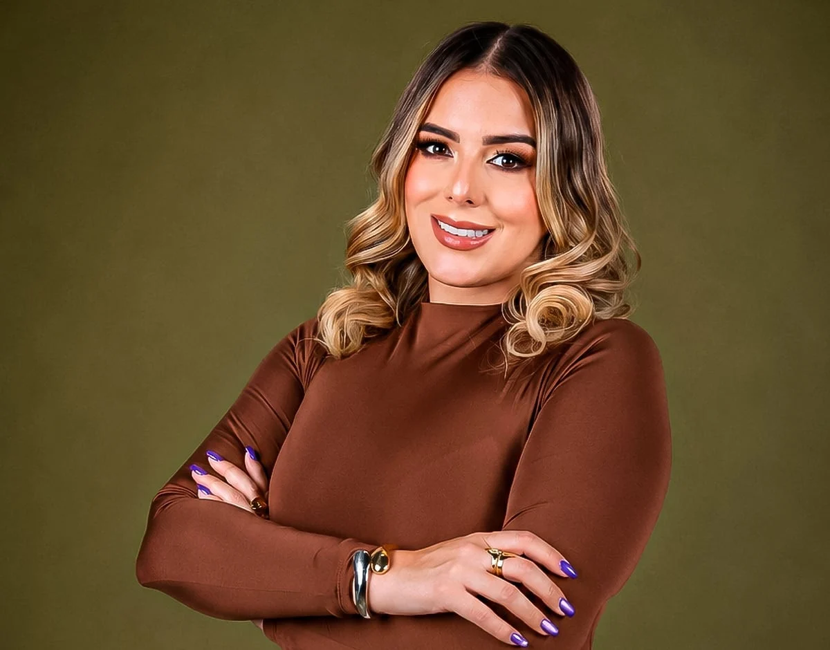 Paula Inspira, con blusa marrón y los brazos cruzados, sobre un fondo verde